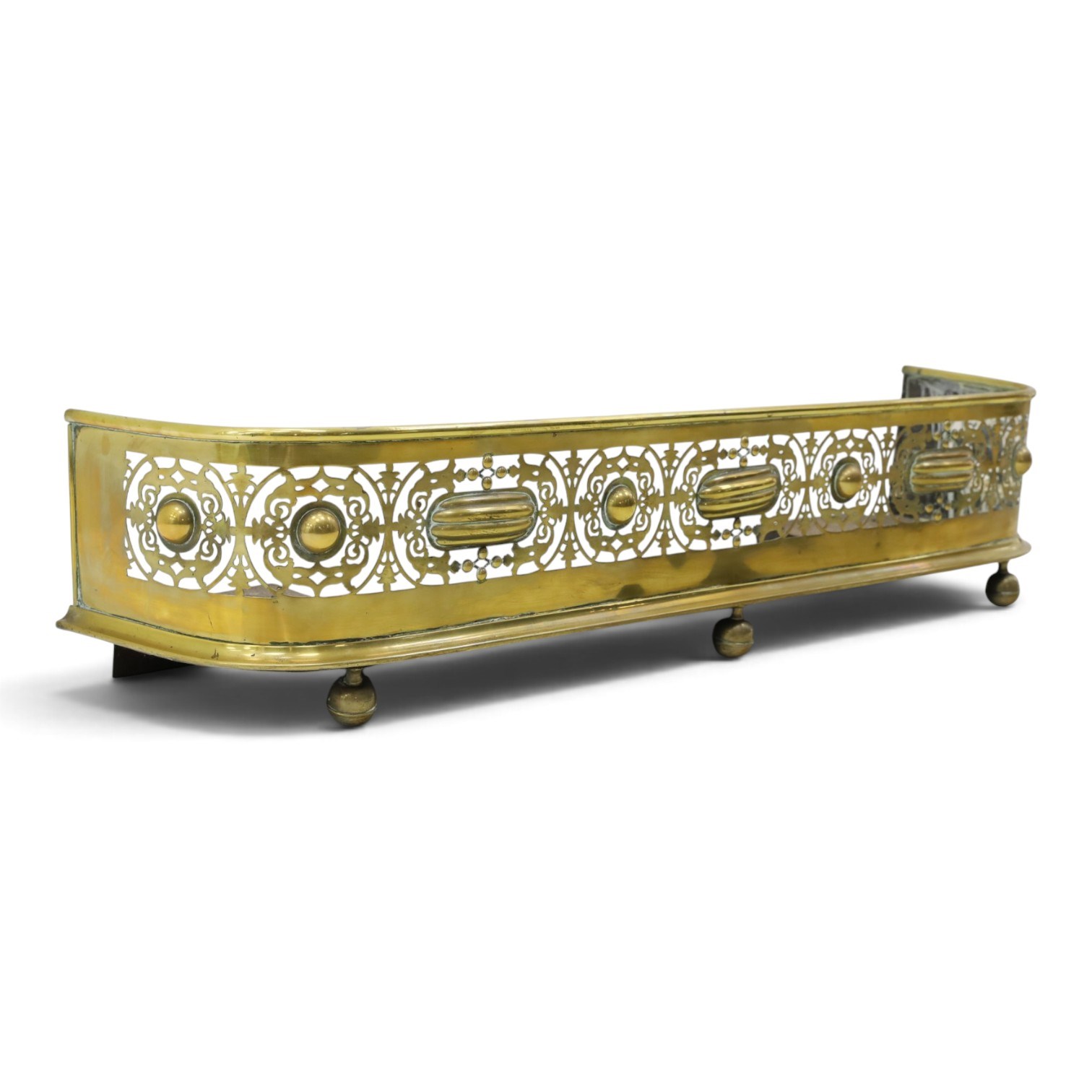 Victorian pierced brass fire fender, the pierced scrolling gallery of Aesthetic taste with applied roundels and protruding lobed mounts, raised on bun feet