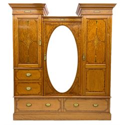 Shapland & Petter of Barnstaple - Edwardian satinwood triple wardrobe, the two projecting dentil cornices with chequered inlaid, the central compartment enclosed by oval mirror with bevelled edge, two panelled doors enclosing linen slides and hanging space inlaid with floral lozenge motifs, fitted with drawers, plinth base, 