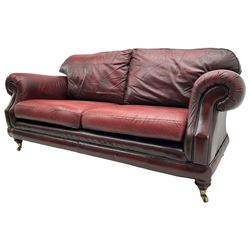 Thomas Lloyd - three-piece lounge suite, comprising of traditional shape two seat sofa (W190cm H80cm) and a pair of wingback armchairs (W100cm H91cm), each with rolled arms over turned supports with brass castors, upholstered in oxblood red leather