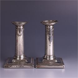 Pair of late Victorian silver mounted candlesticks, the stems embossed with classical ribbon and swag design, upon weighted stepped square bases, hallmarked London 1899, maker's mark worn and indistinct, H12cm