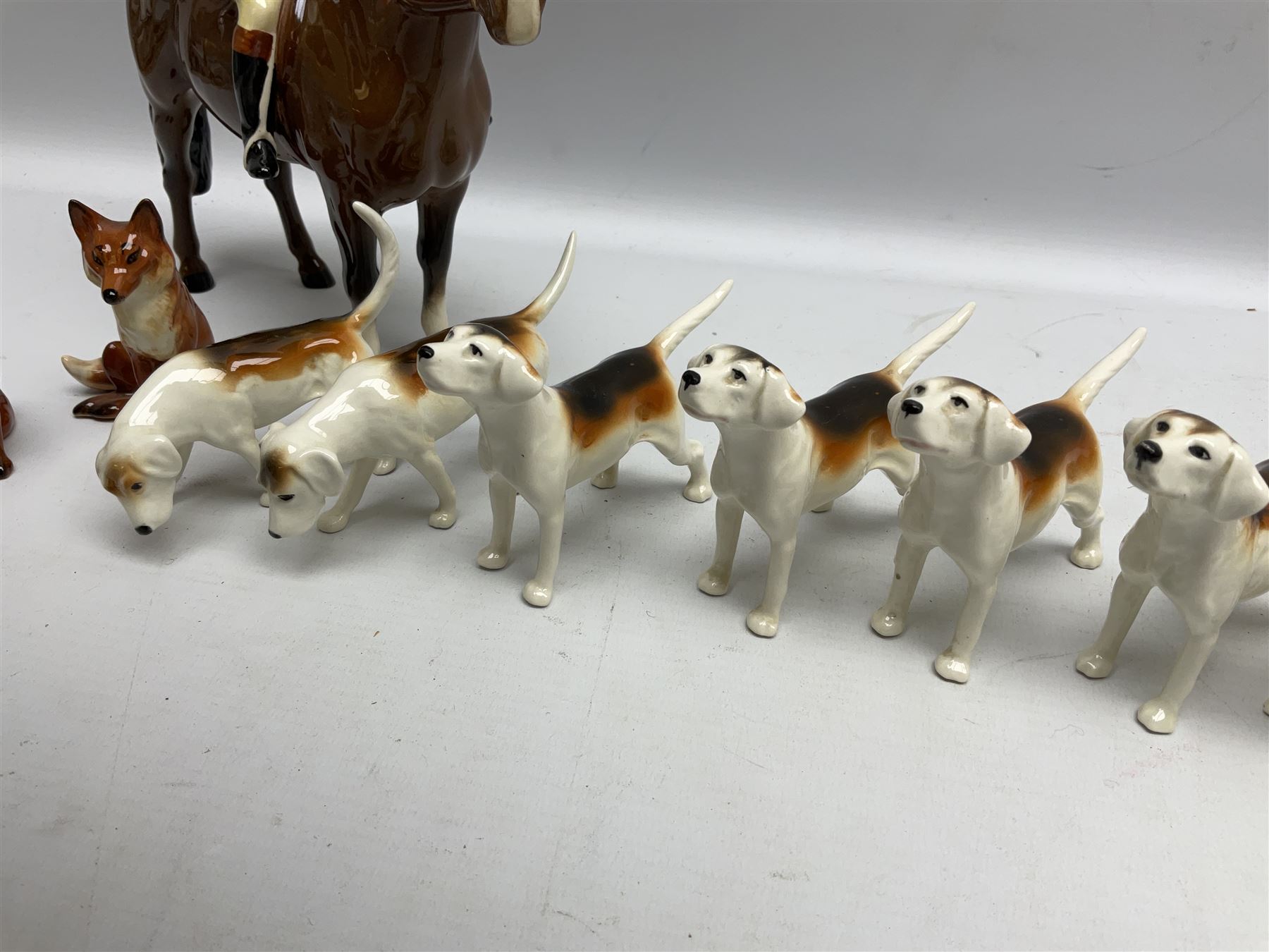 Beswick hunting group, comprising huntswoman on grey horse no 1730, huntsman on brown horse no 1501, two seated fox figures no 1748 and seven fox hounds, all with printed marks beneath (11)
