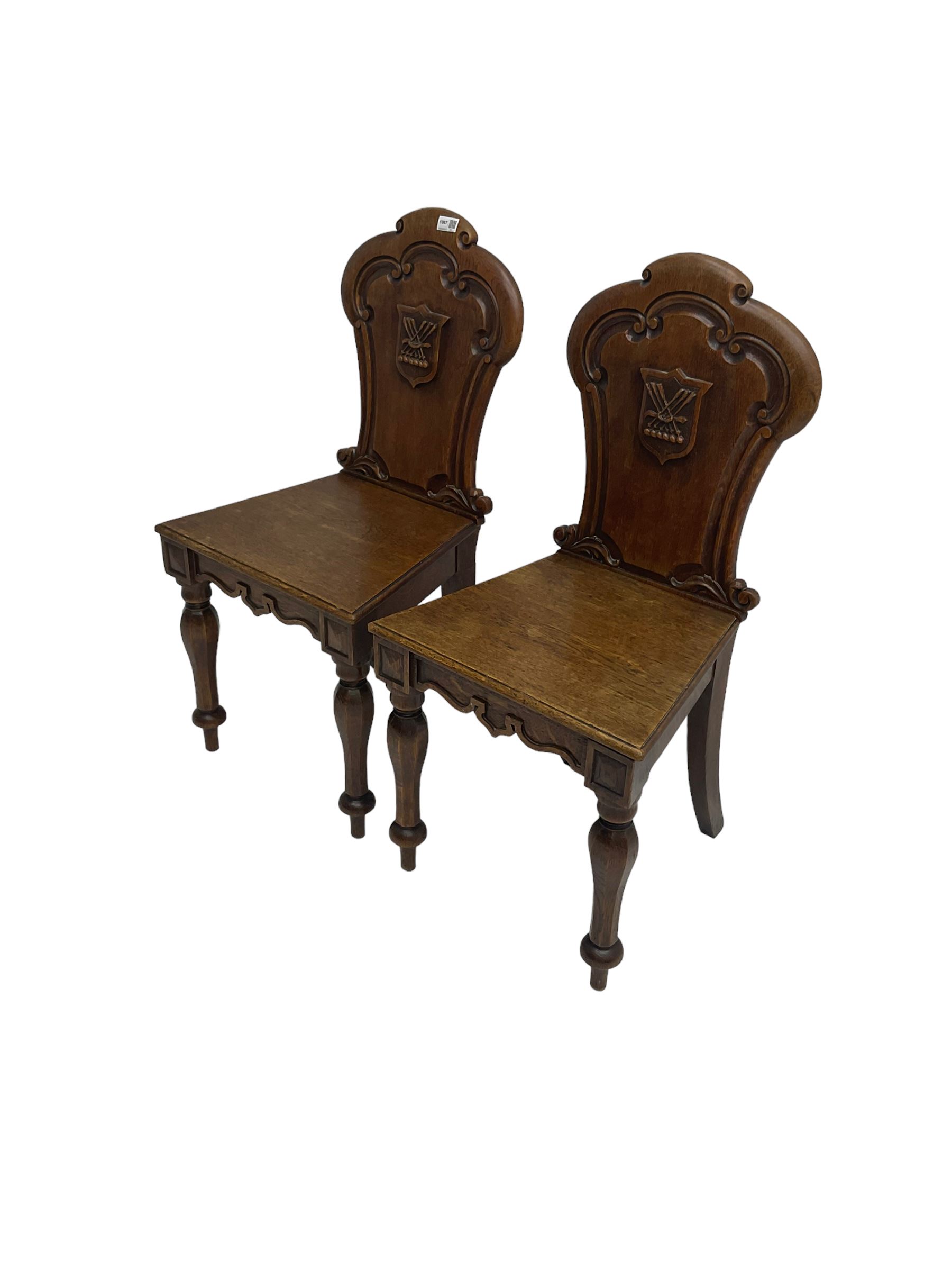 Pair Victorian oak hall chairs, scallop shaped back with carved scrolls and central shield moulding, panel seat over shaped frieze rail, raised on turned supports