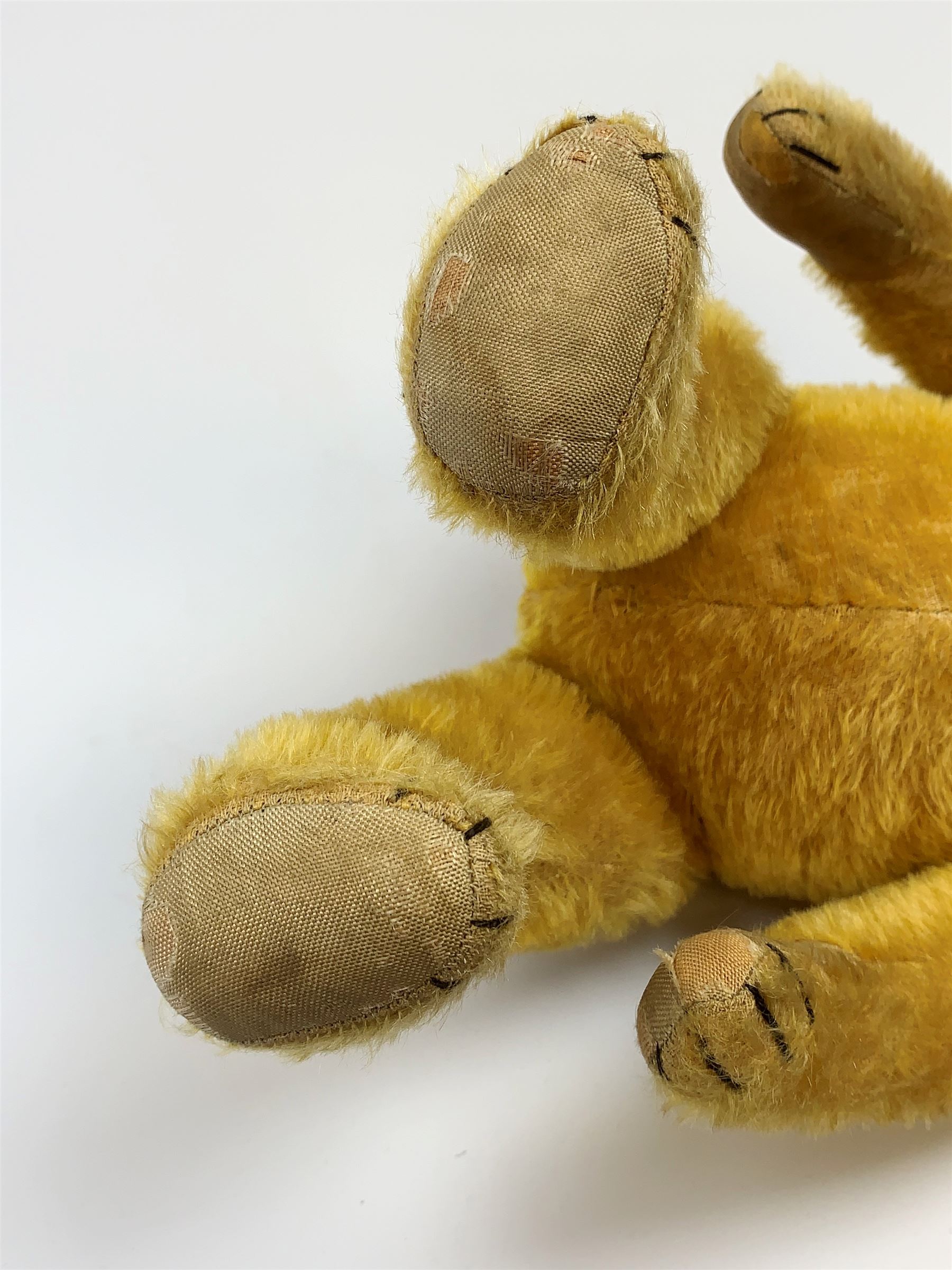Schuco 'yes-no' teddy bear c1925 with wood wool filled short golden mohair body, linen pads with stitched claws and  tail-operated moving head with glass eyes and vertically stitched nose and mouth H18