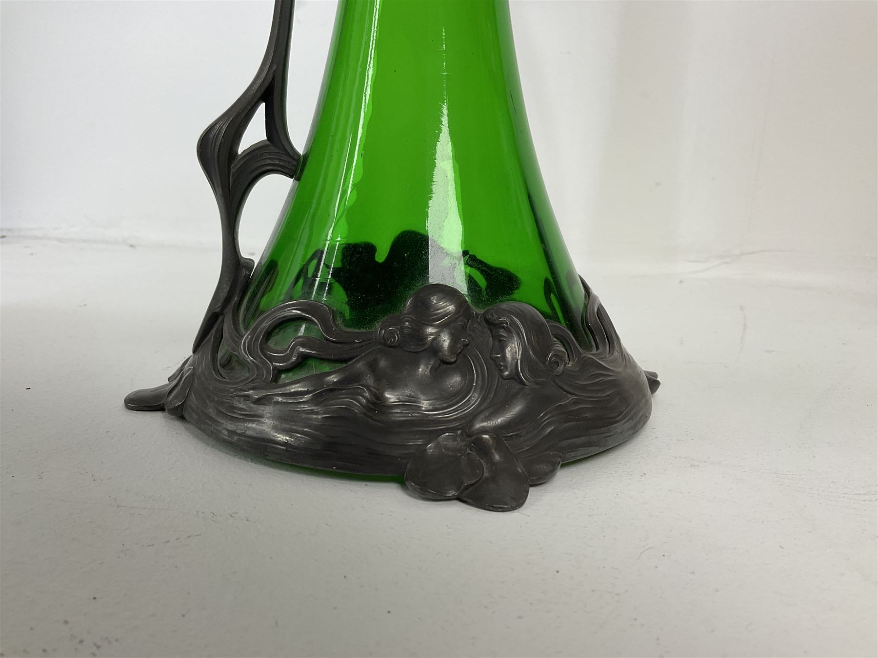 Early 20th century WMF Art Nouveau pewter and green glass ewer, of swept cylindrical form, having a pierced stopper and handle of entwined stems and berry design, the base cast as water nymphs with flowing hair and lily pads, H38cm