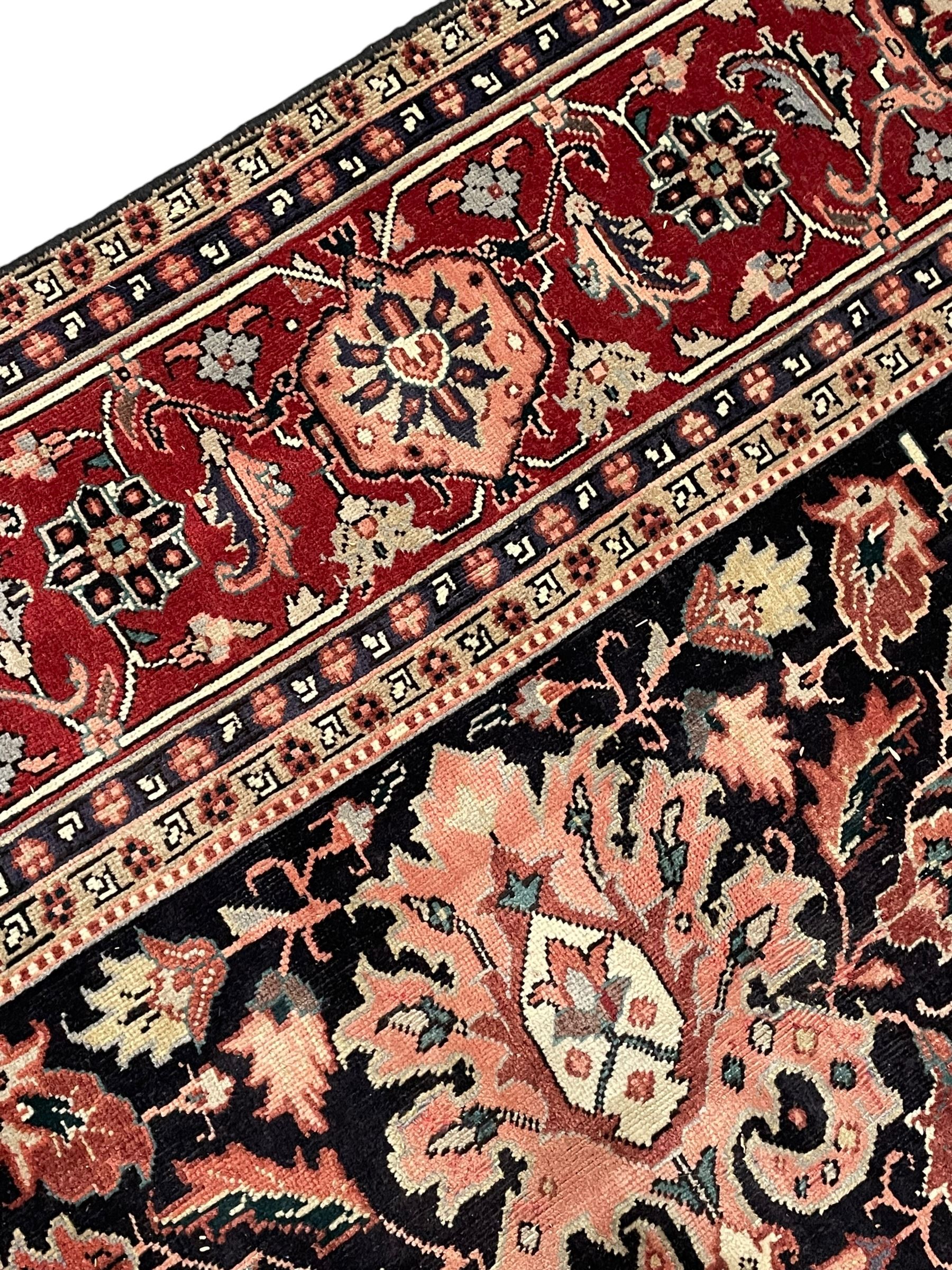 Persian Heriz dark indigo and red ground carpet, the central medallion with large projecting palmette motifs, overall floral design decorated with stylised plant motifs, repeating patterned border within guard stripes