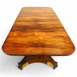 Regency rosewood sofa table, rectangular top with variegated rosewood veneers, hinged D-shaped leaves, over a set of dummy drawers to the back and full-size drawers to the front, with turned knob handles and gilt beaded moulding on frieze above elegant turned, tapering, and fluted, pedestal with a well-carved collar, supported on a large, tripartite concave platform base terminating in richly carved lion paw feet with gilded acanthus leaf carving, on concealed brass castors, circa 1815, length extended 161cm 
