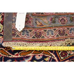 Persian Kashan hand-knotted carpet, madder red ground centred by shaped dark navy and ivory floral medallion with pendants, surrounded by scrolling vines, palmettes and flowerheads, dark navy spandrels, enclosed by dark navy floral border with multiple narrow floral guard stripes