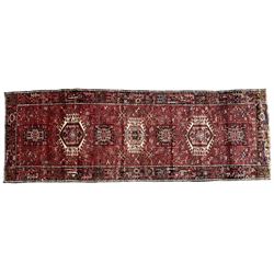Persian Karajeh crimson ground runner rug, the field set with seven geometric lozenge medallions, the field decorated all over with stylised plant motifs, the banded border with repeating geometric shapes and patterns