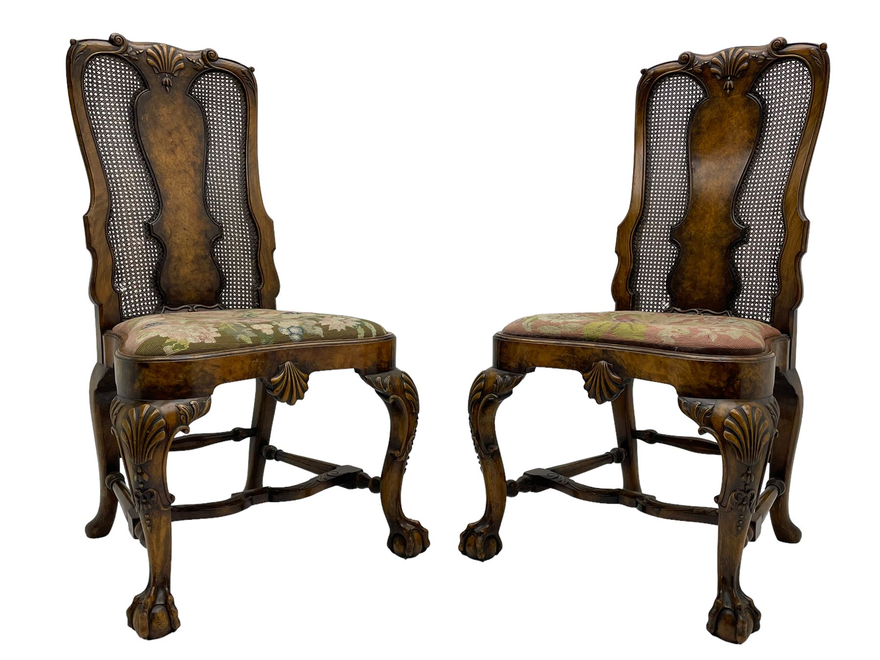 Pair of early 20th century Queen Anne design chairs, the cresting rail carved with scroll and central shell motif, shaped uprights and splat encased in cane work panels, shaped moulded seat frame with shell motif, floral needlework upholstered drop-in seat cushion, on shell carved cabriole supports with ball and claw feet, united by turned and shaped middle stretcher carved with acanthus leaf
