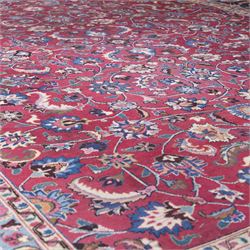 Persian Mashad design wool carpet, the red ground with dense scrolling floral and foliate decoration, within dark blue main border decorated with repeating palmettes and shaped leaves