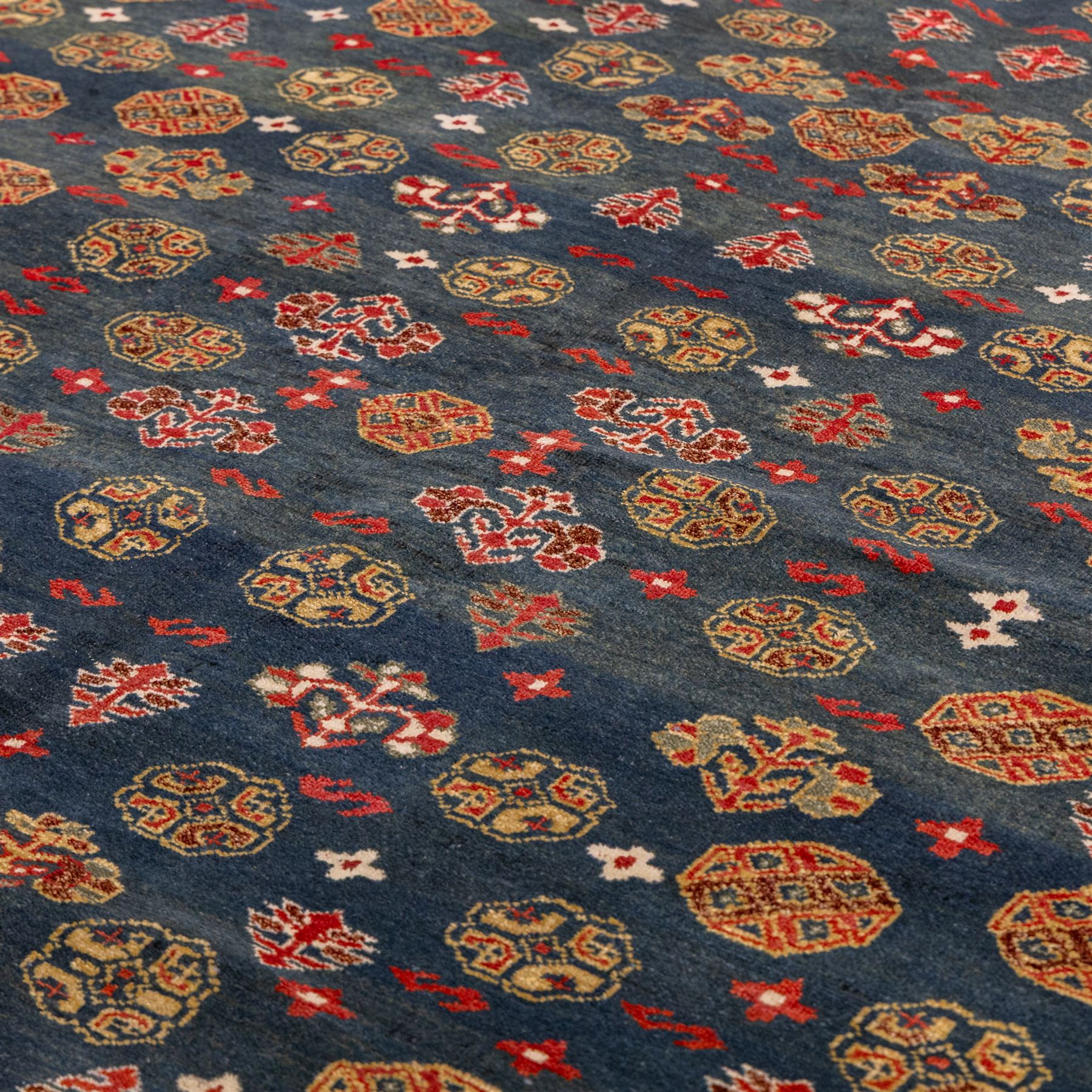 North East Persian Turkoman hand-knotted rug, deep teal blue field decorated with repeating rows of stylized octagonal guls and cruciform tribal motifs arranged in a lattice formation, enclosed composition featuring angular devices and reciprocal motifs, with cotton fringe ends