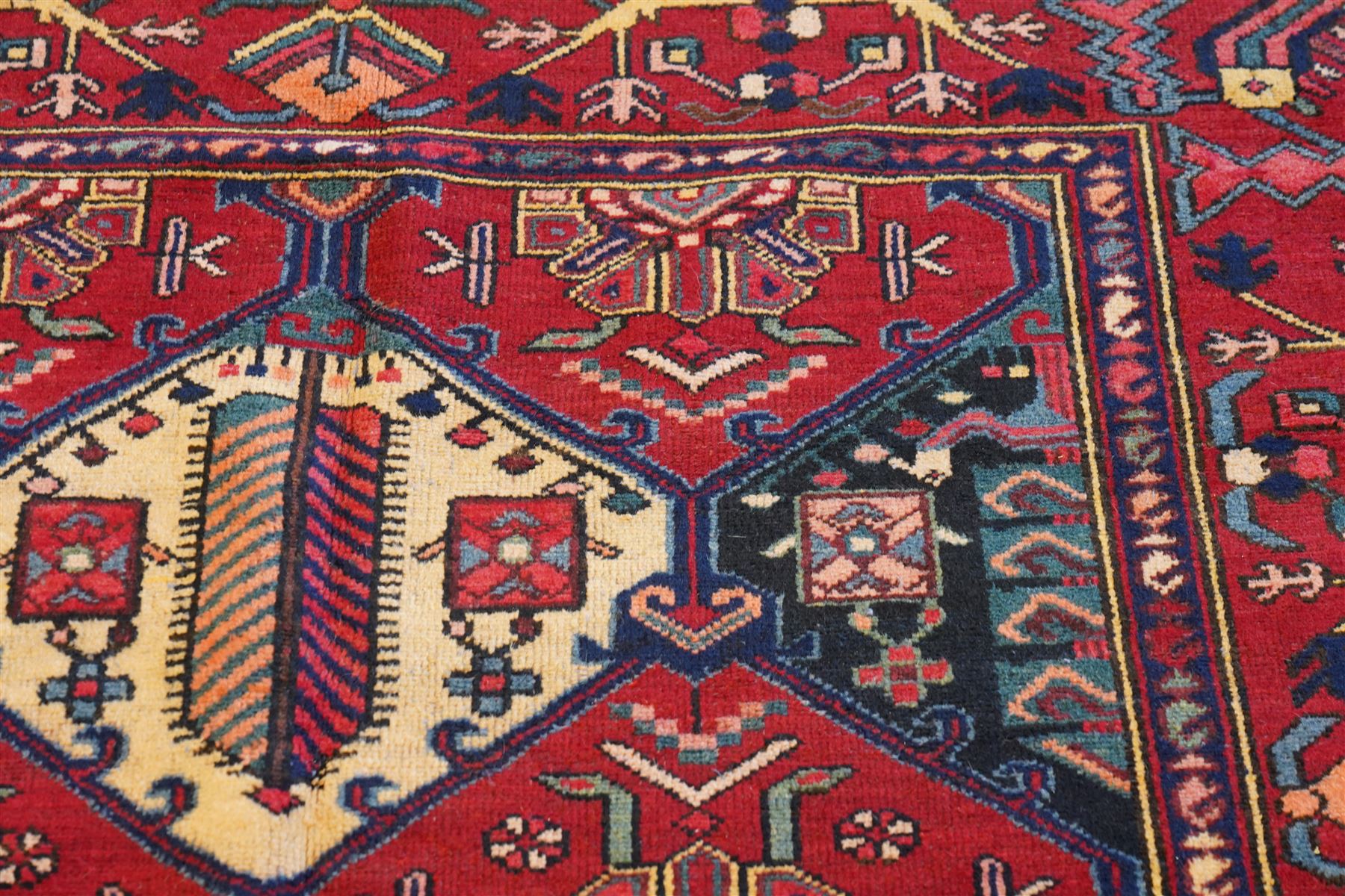 North West Persian Heriz hand-knotted rug, madder red field with an all-over lattice of stepped lozenge medallions enclosing stylized geometric floral motifs and ivory reserve panels, framed by angular vinery and motif borders, main border with with stylized rosettes and geometric devices, flanked by narrow guard stripes,, cotton fringe ends 