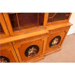 Sheraton Revival satinwood breakfront bookcase, frieze painted with scrolling leafage above four astragal doors with adjustable shelves, the base with four doors painted with floral sprays in oval panels, on a plinth base, W234cm, H235cm, D52cm