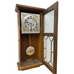 German - Art Deco oak cased 8-day wall clock c 1930, with a moulded flat top and fully glazed door, deeply cut bevelled glass panels and visible pendulum, silvered dial with Art Deco design spandrels, Arabic numerals, minute track and spade hands, twin train movement striking the hours and half hours on four gong rods. With pendulum and key.  