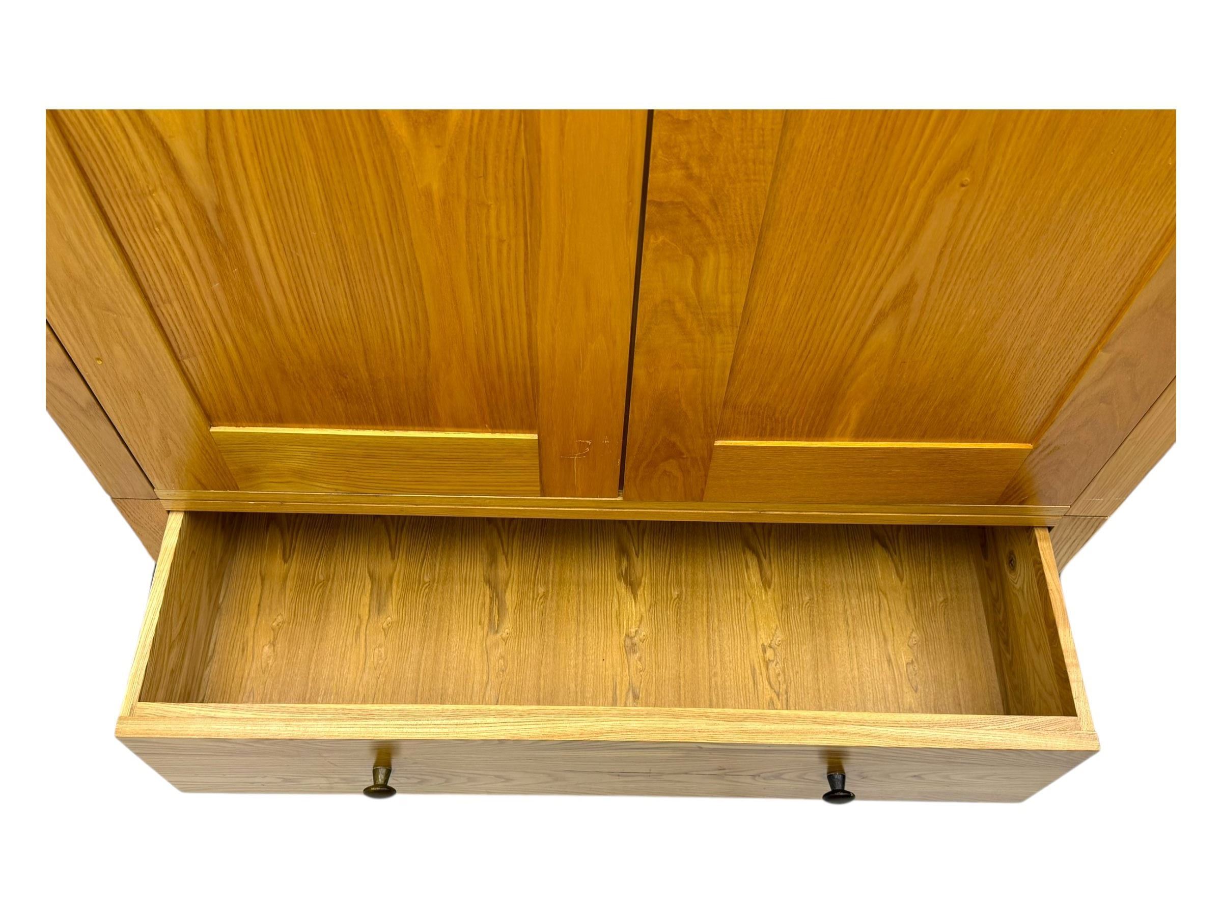 Contemporary light oak double wardrobe, projecting cornice over two panelled doors enclosing hanging rail and shelf, above full-width drawer, on shaped stile supports