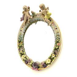 A late 19th/early 20th century Sitzendorf mirror, with encrusted flowers to the oval frame, surmounted by two putto, H34cm D25cm.