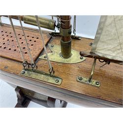 Early 20th century large pond yacht with mahogany hull, stained pine keel with brass rudder, simulated deck hatches and brass fittings, rigged as a staysail schooner (?) with four sails L117cm H148cm; loose mounted on stained pine stand
