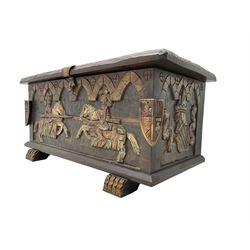 Carved wooden blanket chest, the tooled hinged lid with shaped metal strap hinges and catch, the front carved with arcade over two medieval jousters, on carved sledge feet