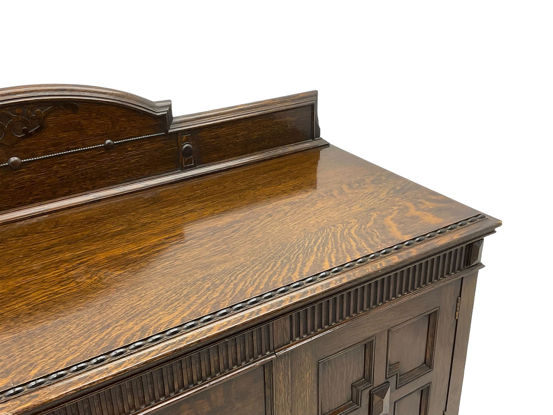Early 20th century oak sideboard, raised stepped arch back over moulded rectangular top, fitted with two drawers and two panelled cupboards with geometric mouldings, on turned and lobe carved baluster feet united by stretchers 