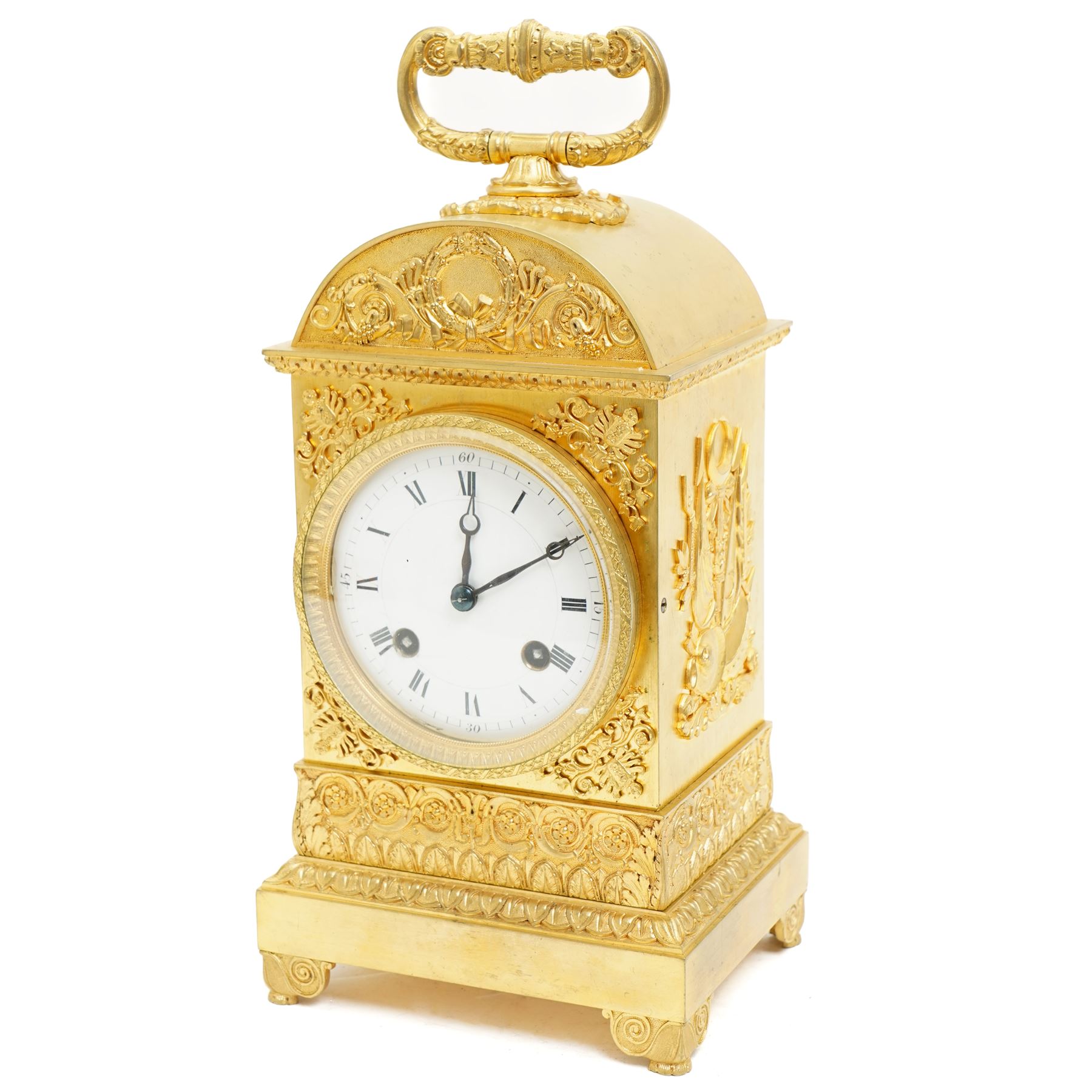 Fine Swiss ormolu 8-day early 19th century Pendule d'Officer style clock c1820,  circular double train ting-tang movement striking the quarters on a graduated pair of bells and sounding the hour on one, going train with a vertical platform lever escapement and over sprung balance, rack striking, with visible hour and quarter strike work to the backplate, movement unsigned, convex enamel dial with Roman numerals and steel moon hands behind a glazed gilt bezel, case with a scroll cast handle to the arched top with applied rococo decoration to the tympanum, both sides of the case adorned with a military trophy of arms motif and deep frieze with foliate arcading beneath, on a rectangular plinth with decorative scroll engraved bracket feet. With Key.   