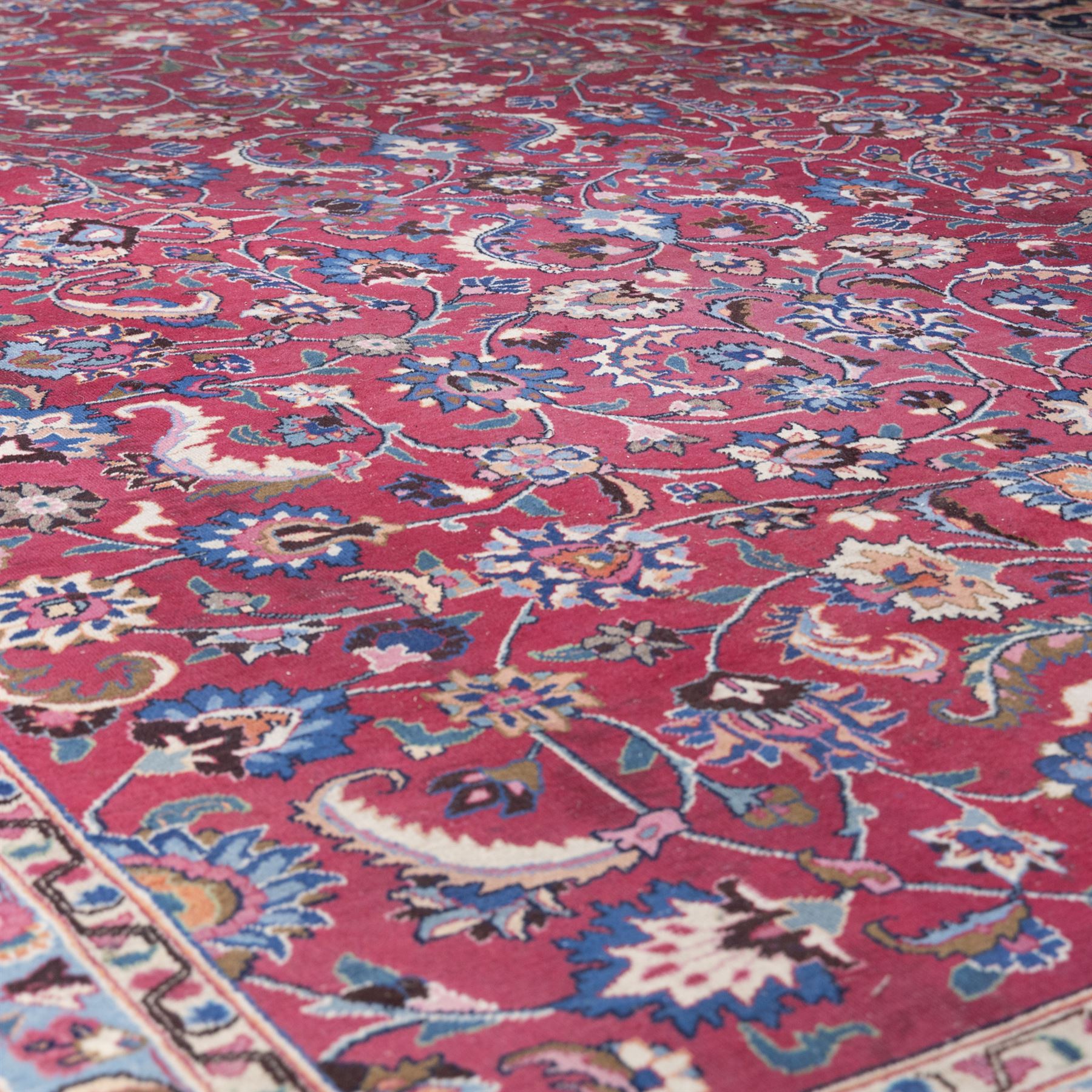 Persian Mashad design wool carpet, the red ground with dense scrolling floral and foliate decoration, within dark blue main border decorated with repeating palmettes and shaped leaves