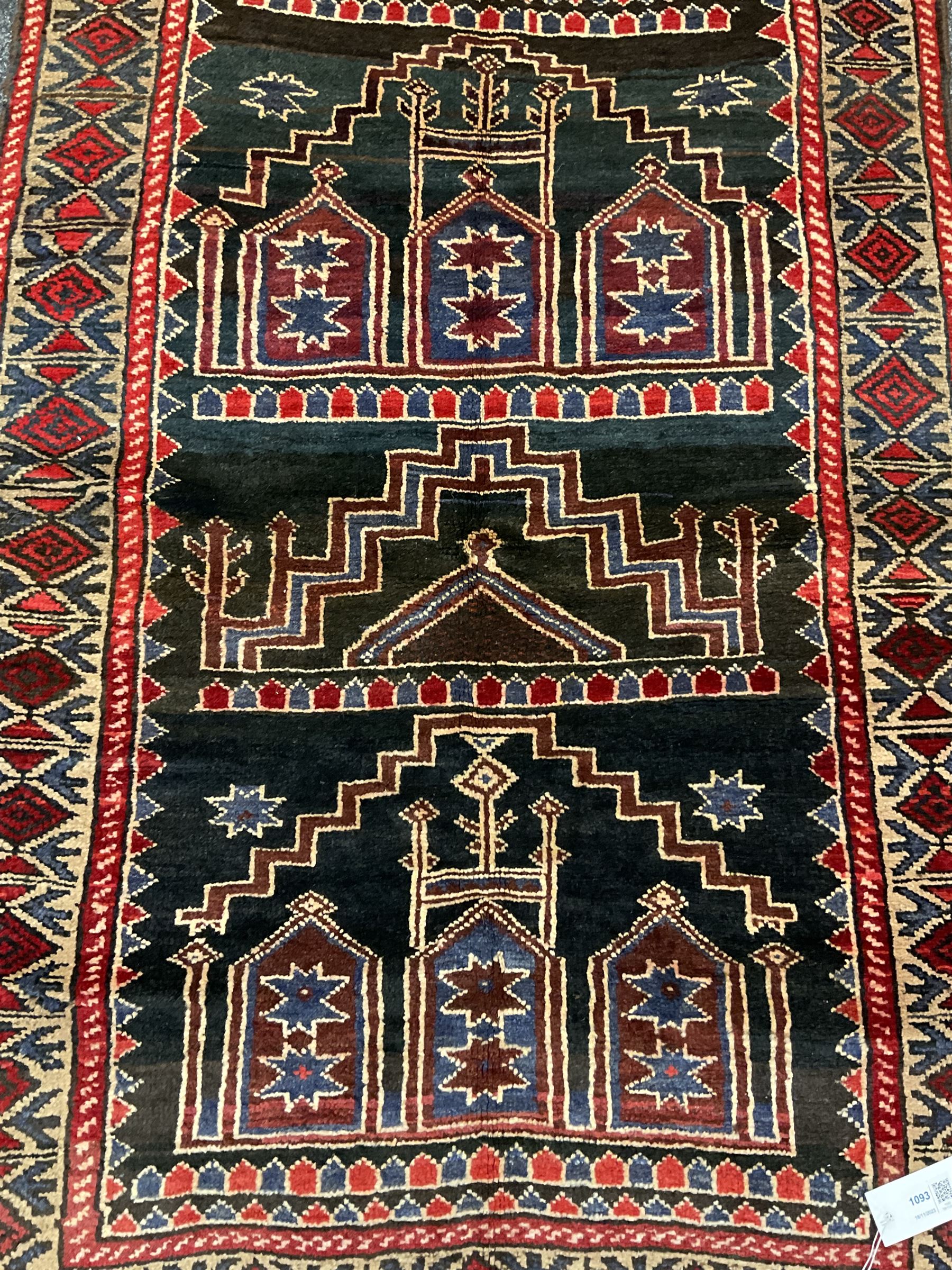 Baluchi dark indigo and crimson ground rug, decorated with cityscape within geometric border 