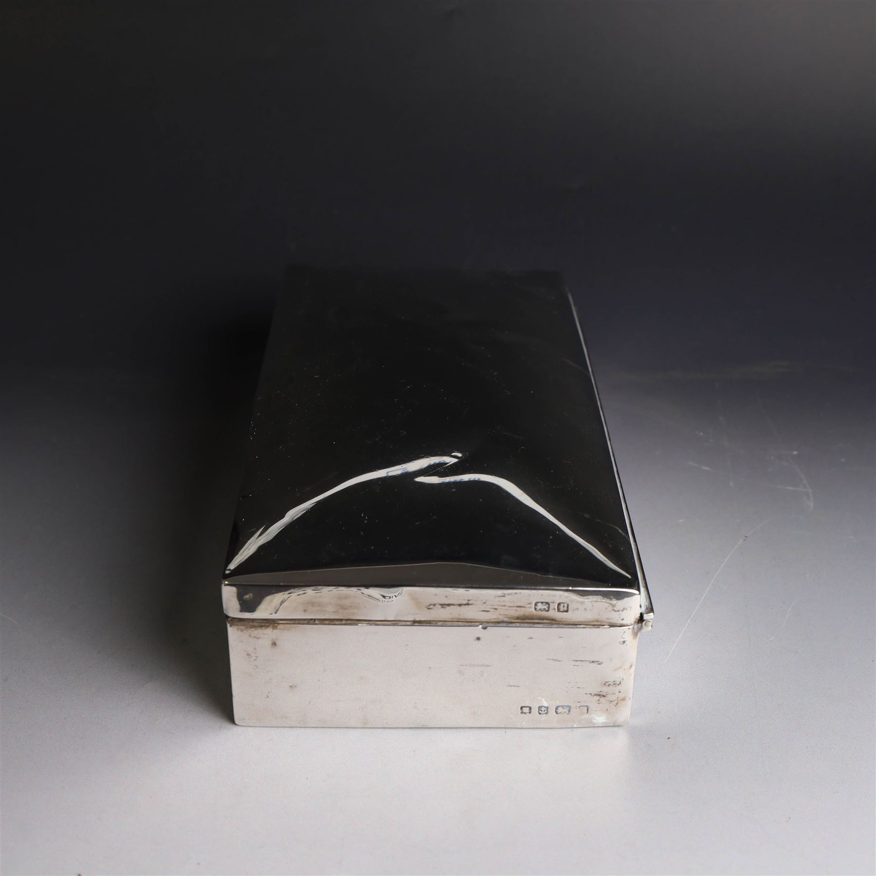 Two silver cigarette boxes, comprising early 20th century plain rectangular example with compartmentalised softwood interior, hallmarked Birmingham 1914, maker's mark indistinct, and an early 20th century example with engine turned decoration and engraved initials to cover, hallmarks worn and indistinct, largest H4.5cm, W21cm