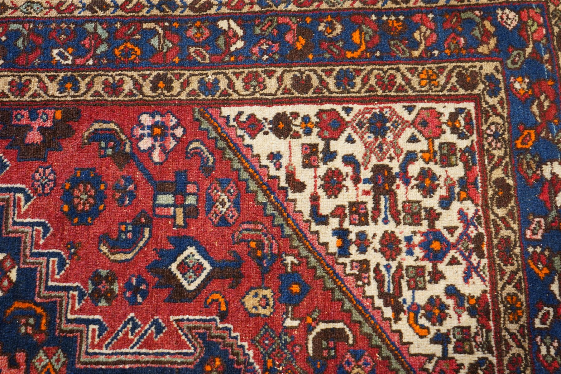 Persian Heriz crimson ground carpet, the central navy geometric medallion on a red crimson ground field, surrounded by further geometric stylised motifs and foliate designs, enclosed by multiple guard-lines  