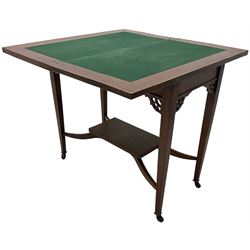 Edwardian inlaid mahogany games table, the rectangular fold-over swivel top decorated with central shell motif inlay and ebony stringing, raised on tapering supports united by shaped X-stretcher and undertier