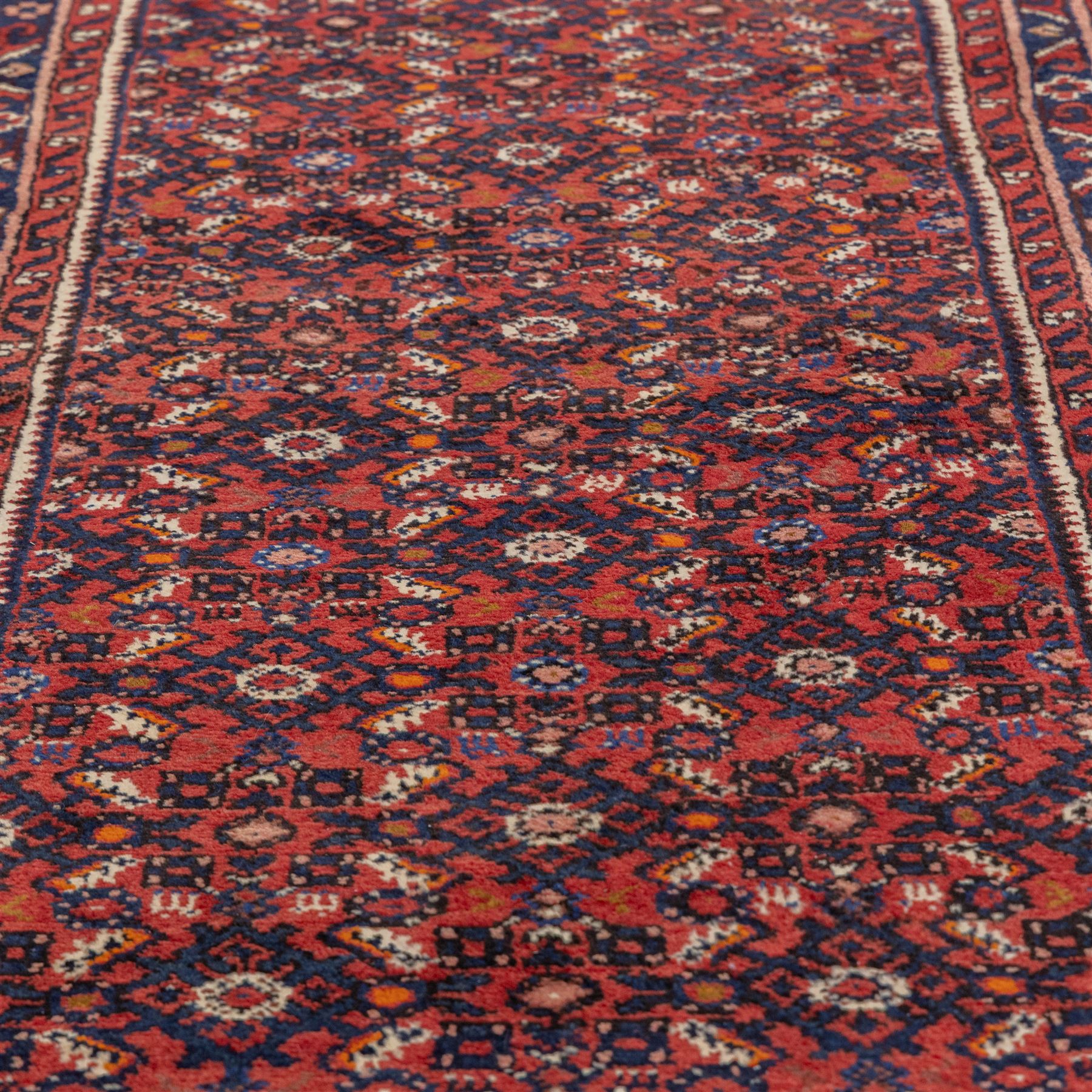 North West Persian Malayer hand-knotted runner, decorated with a dense all-over pattern of small repeating boteh and rosette motifs on a rich madder red ground, field filled with geometric floral elements arranged in a lattice design, framed by a narrow main border and flanked by slender guard borders, with cotton fringe ends 