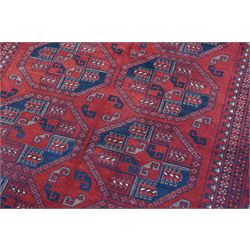 Afghan red ground Bokhara rug, the field decorated with two rows of large Gul motifs, within geometric pattern borders 