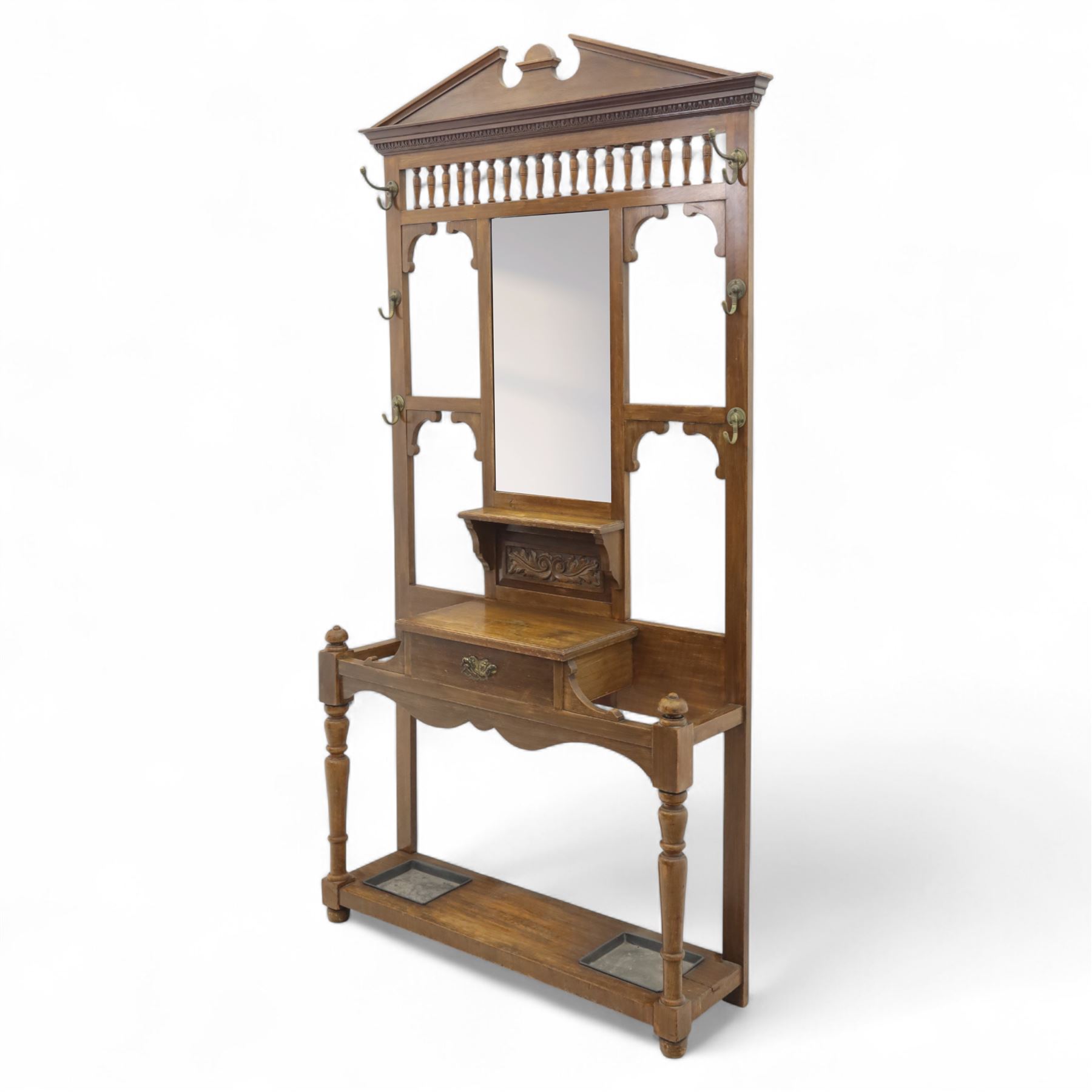 Edwardian walnut hall stand, the shaped pediment above turned spindle gallery and bevelled mirror, fitted with brass double coat hooks, single drawer with cast handle and carved frieze, flanked by turned supports, lower platform fitted with twin metal drip trays