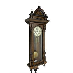 German - late 19th century mahogany 8-day Vienna regulator, with an arched pediment with turned finials, fully glazed door flanked by reeded pilasters with carved capitals, ogee base with conforming turned pendants, two part enamel dial with Roman numerals, minute track and seconds dial, weight driven movement striking the hours and half hour on a coiled gong.  With weights and pendulum.