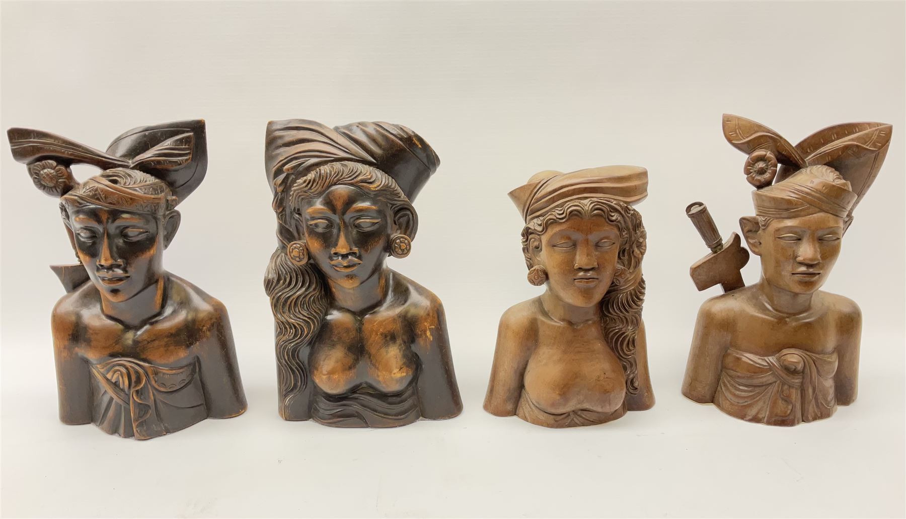 Two pairs of Balinese carved wooden bust figures of a man and woman, with elaborate head dresses, along with other wooden carved figures, a small barometer and a framed print. 