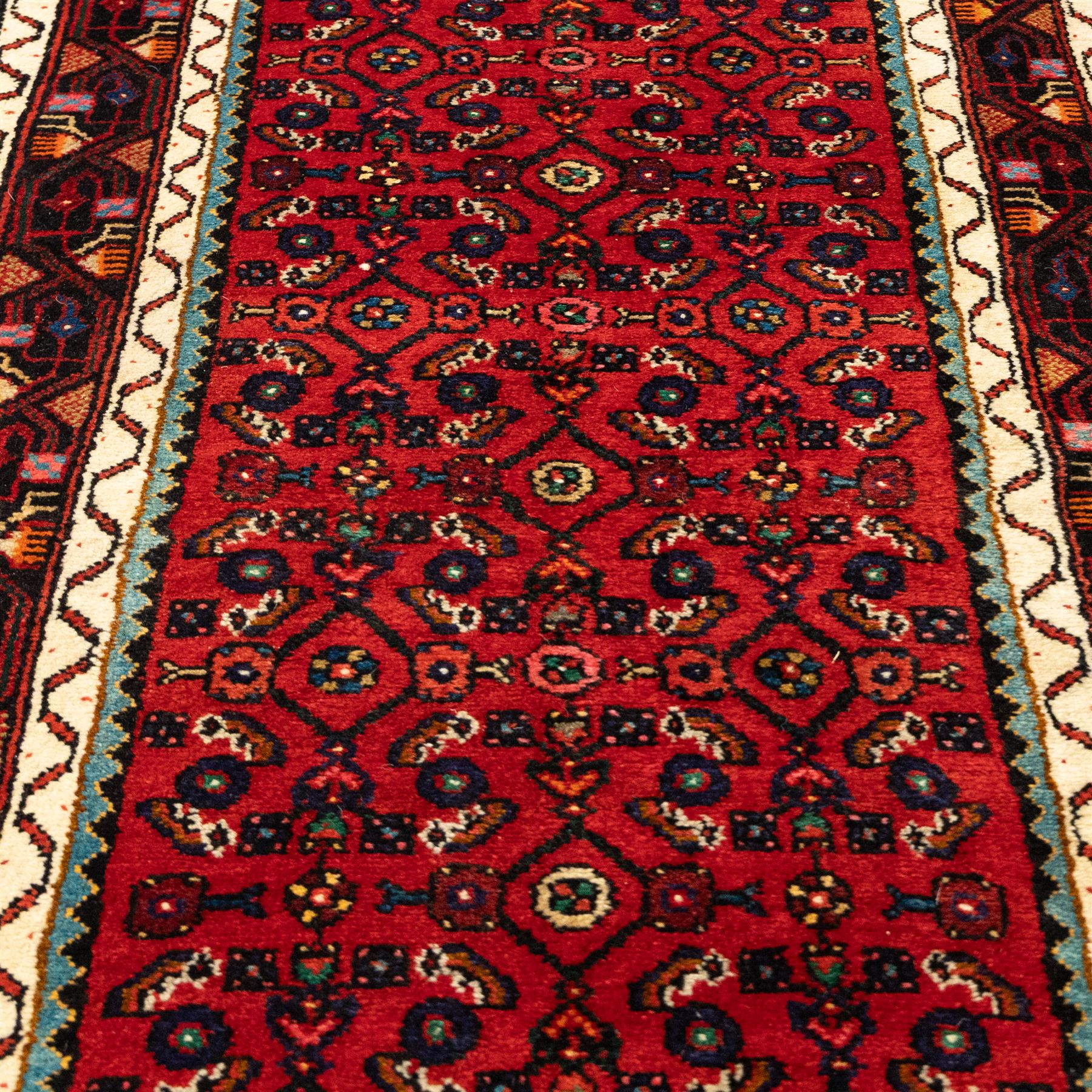 North West Persian Malayer runner, madder red field decorated with an all-over design of stylized herati motifs in shades of indigo, ivory, and green within ivory and dark blue borders of angular vine and rosette design, with cotton fringe ends 