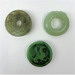 Two jadeite bi discs, largest D5.5cm, together with a nephrite jade disc with carved zoomorphic detail, D5cm. (3). 

