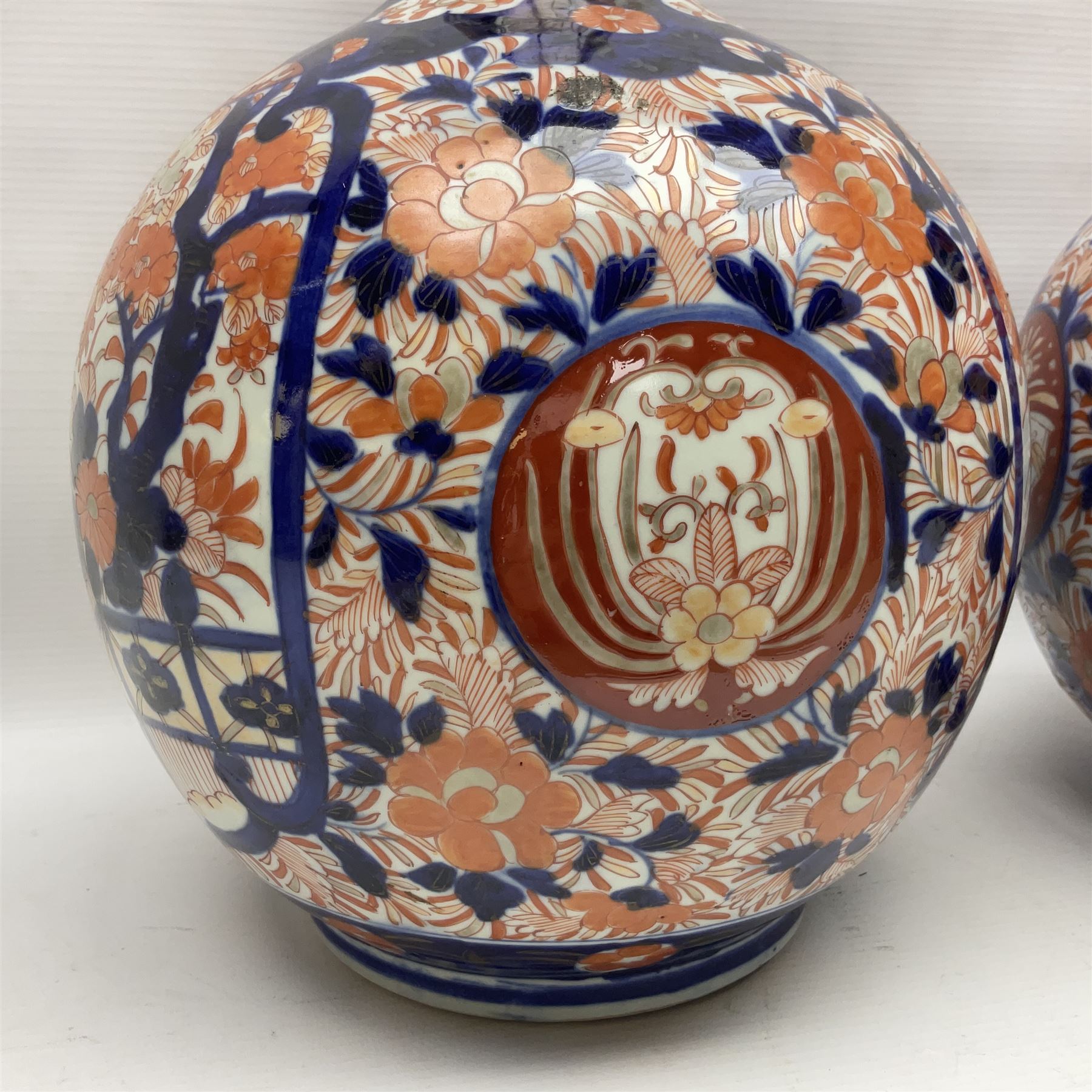 Pair of large 19th century Japanese Imari porcelain bottle vases, painted with shaped reserves of peonies, chrysanthemums and prunus blossom, each H46cm