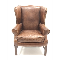  George lll  style wing back chair,  upholstered in brass nailed antique brown leather with loose seat cushion on square supports joined by stretchers  