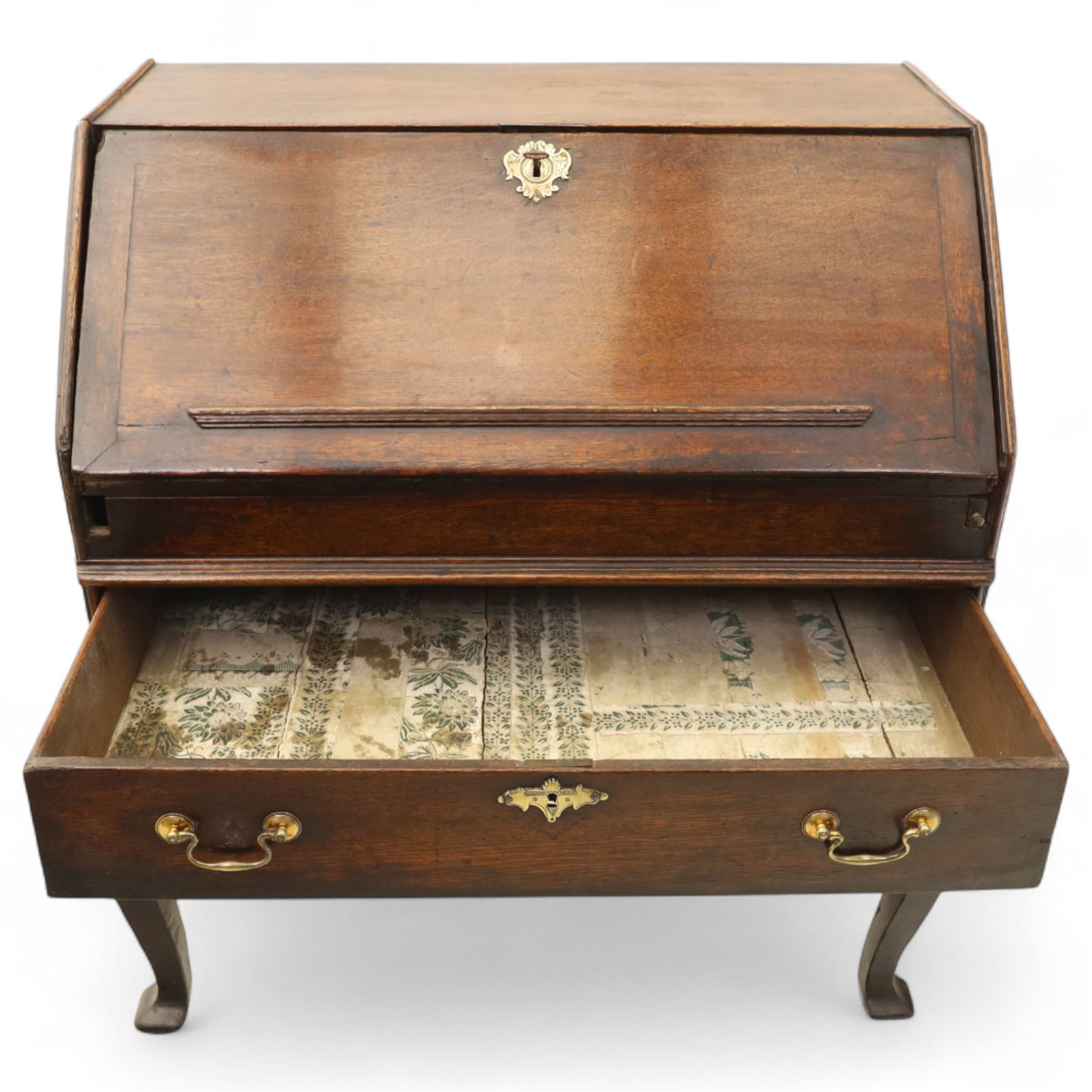 Early 18th century George I oak bureau on original stand, the fall front enclosing an arrangement of correspondence drawers and pigeonholes over central well, fitted with single long drawer below, the shaped apron over cabriole supports with pad feet