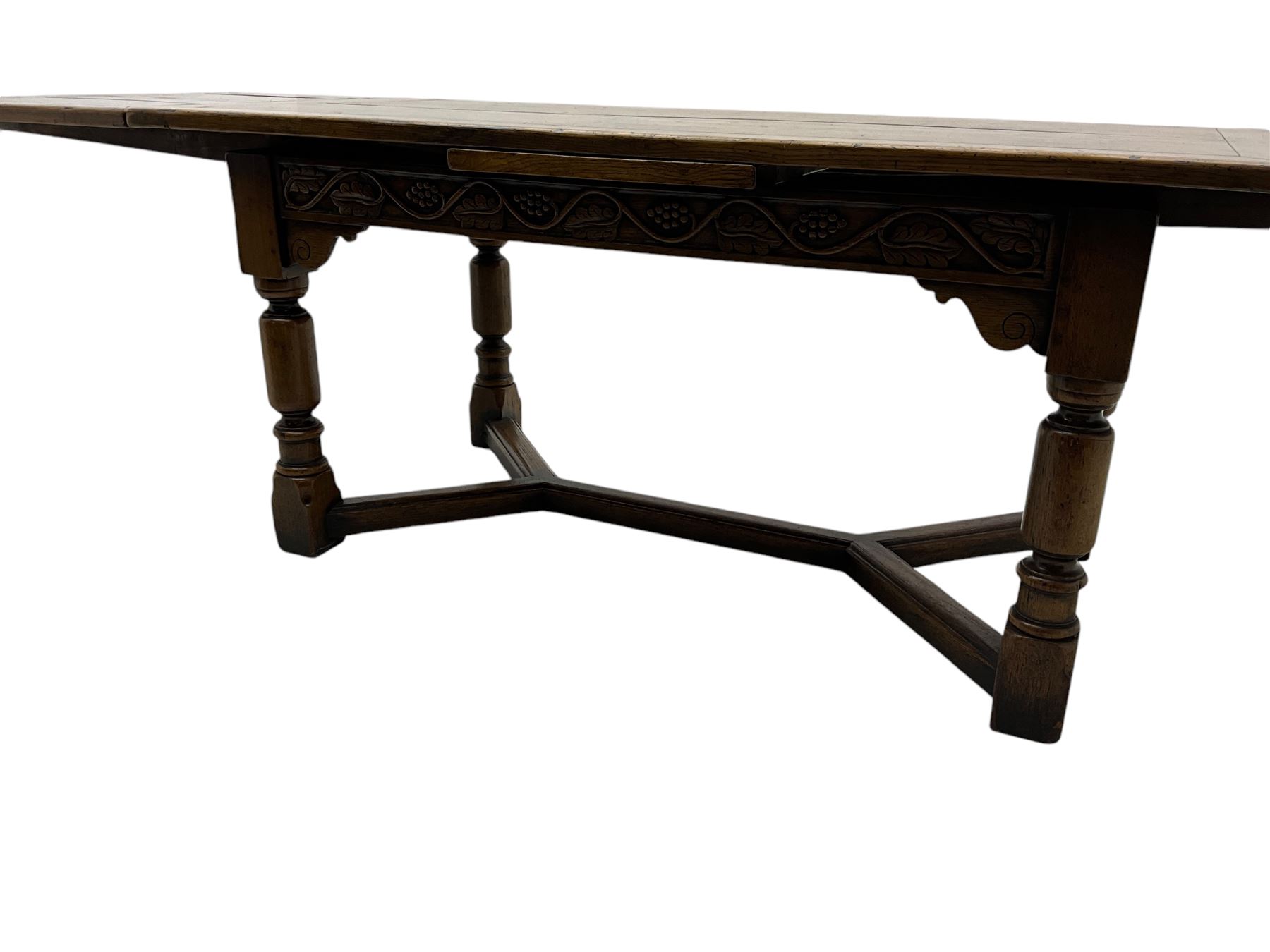 Early 20th century Jacobean design draw-leaf oak dining table, rectangular top with carved frieze depicting scrolling foliage and grape clusters, sliding extending leaves, raised on robust turned supports united by H-stretcher  