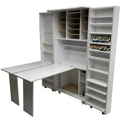 Large white finish sewing cabinet, enclosed by two doors fitted with thread holders and shelves, the interior fitted with shelves and sliding trays, with fold down work surfaces 