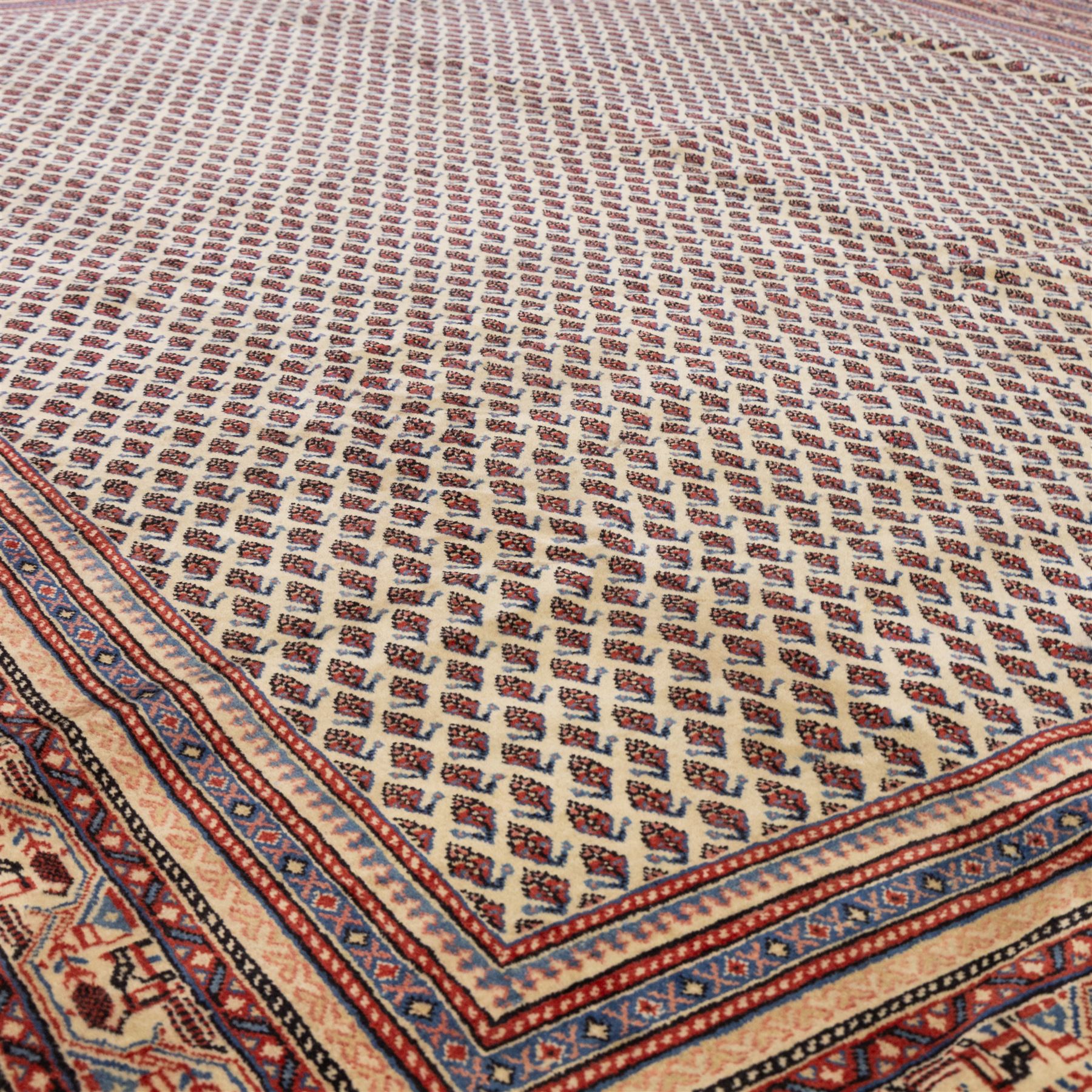 North West Persian Boteh-Mir hand-knotted rug, madder red field decorated with an all-over lattice of small boteh motifs and a central stepped lozenge medallion with repeating stylized boteh and geometric devices, spandrels similarly worked, with multiple narrow borders of floral and geometric bands, in tones of madder red, indigo blue, ivory, and soft green, with cotton fringe ends