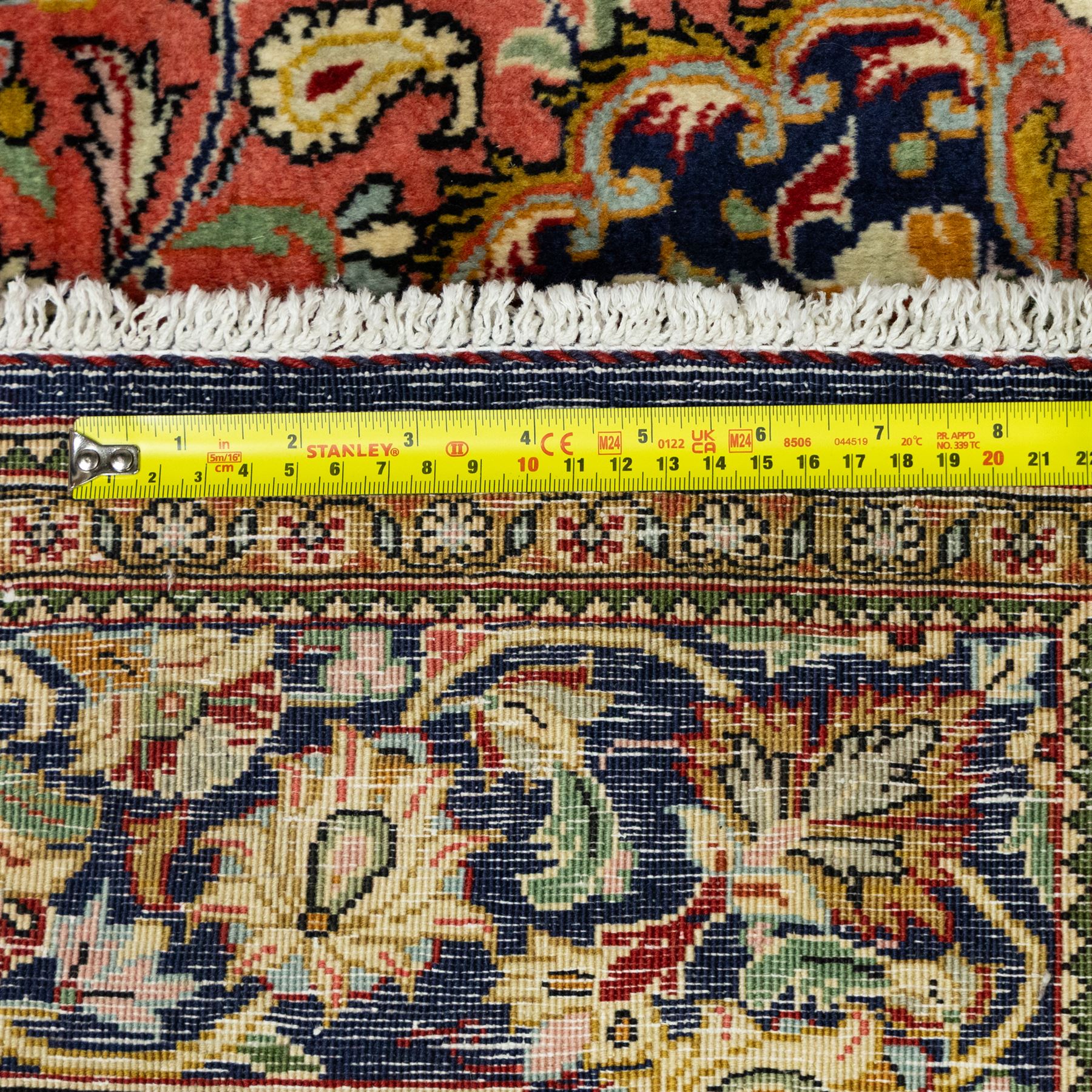 Central Persian Qom hand-knotted carpet, salmon pink ground, with a central dark navy shaped floral medallion with pendants, surrounded by dense scrolling foliate and floral motifs incorporating rosettes, palmettes and delicate vine work, enclosed by ivory spandrels and a dark navy border with repeating palmettes and meandering vines, flanked by narrow floral guard stripes, with cotton fringes