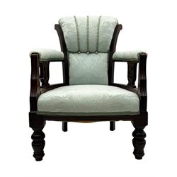 Late Victorian carved mahogany open armchair, the shaped back with fluted upholstered panel and padded arms above pierced scroll carved side supports, over a broad upholstered seat, on turned front supports