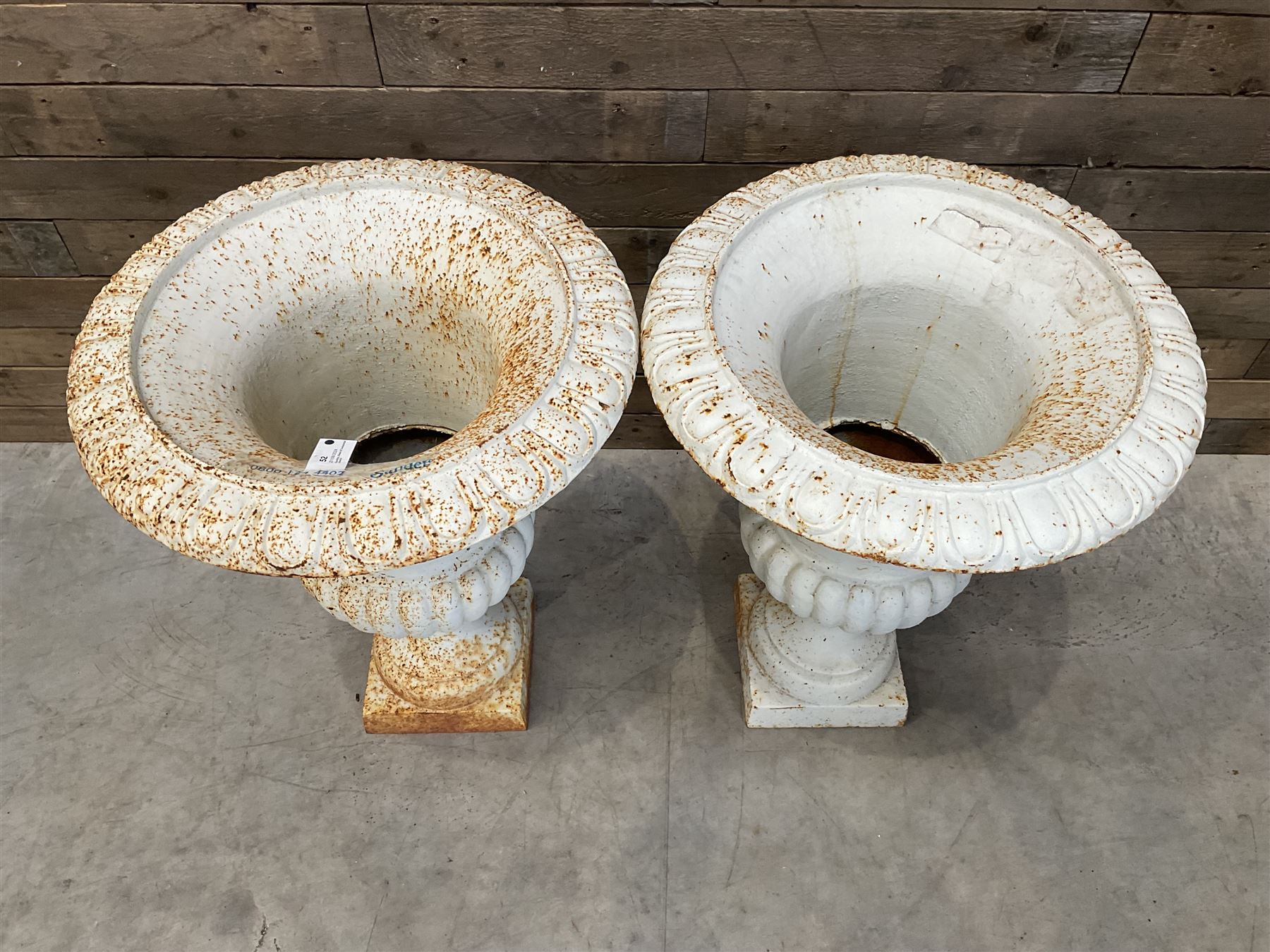 Pair of large Victorian design white painted cast iron campana shaped garden urns, egg and dart rim over a gadrooned underlobe, tapering column on square plinth base