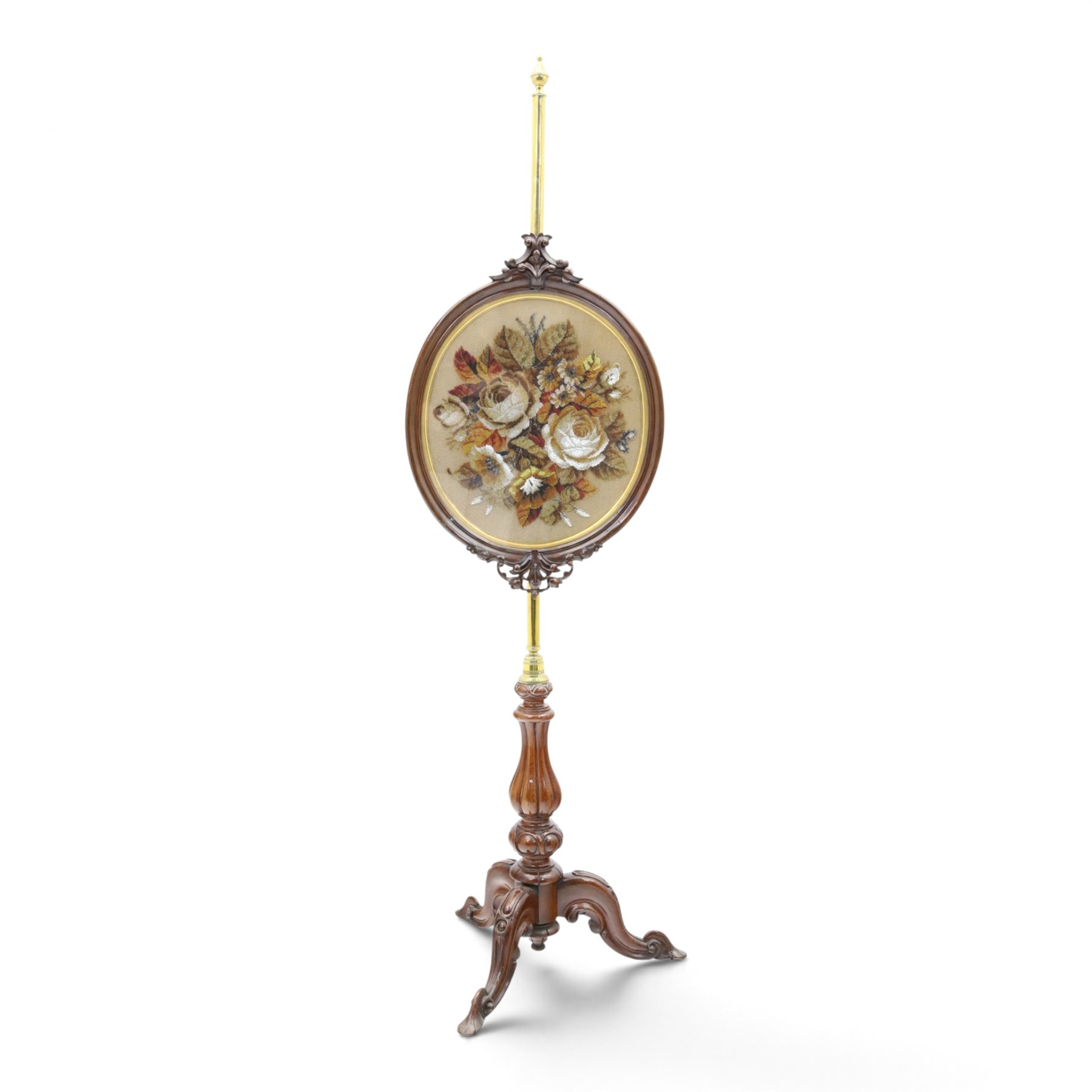 Two Victorian mahogany pole screens, comprising an oval example with floral needlework panel and carved cresting, on brass pole and tripod base with scroll carved supports (H 153cm, W 43cm, D 43cm); and a rectangular example with glazed architectural print panel, on brass pole, turned column and conforming scroll carved tripod base (H 147cm, W 38cm, D 38cm)