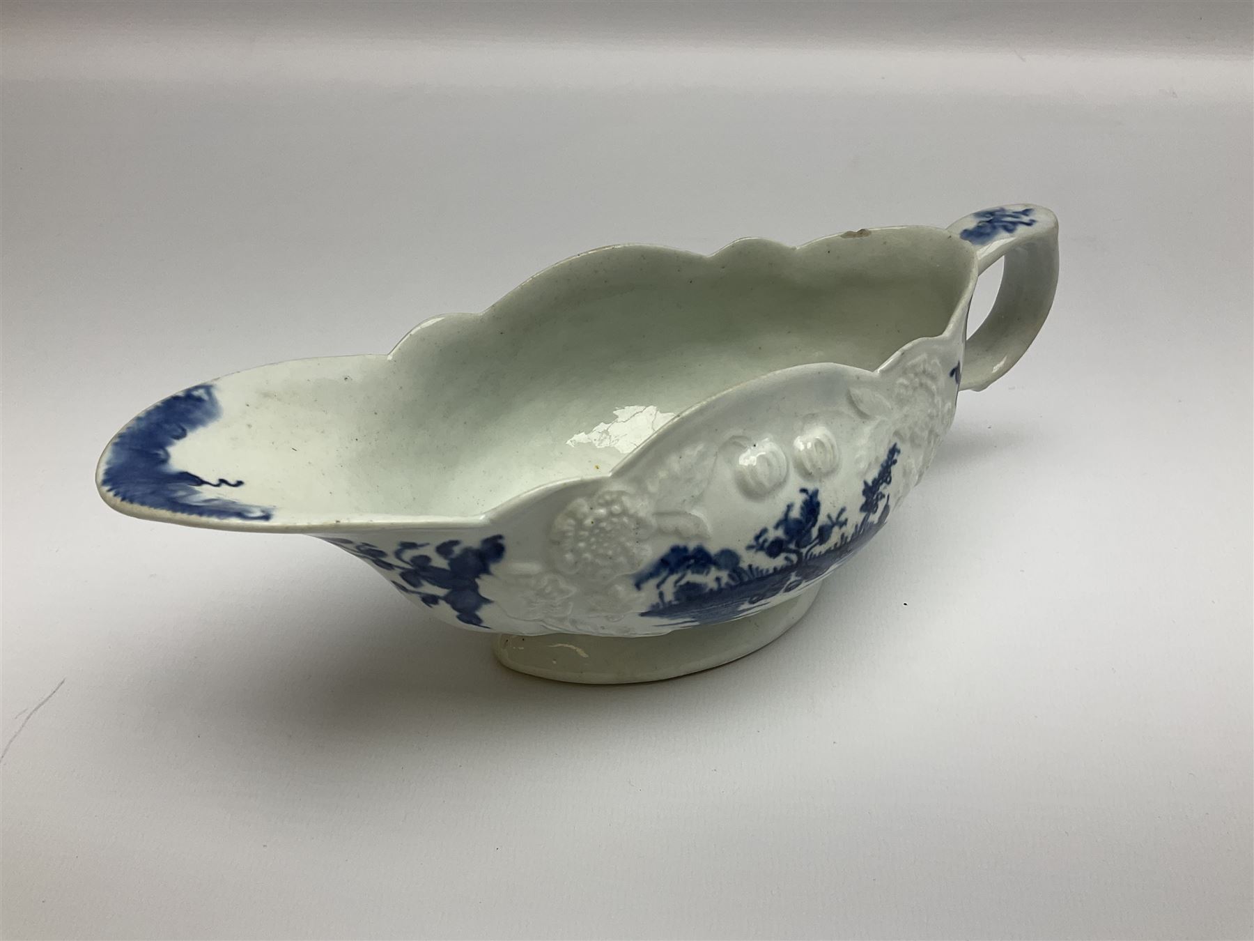 Large 18th century Lowestoft sauce boat, circa 1770, the body decorated with Hughes type floral moulding, and painted in underglaze blue with an Oriental landscape, and foliate sprigs, L23cm