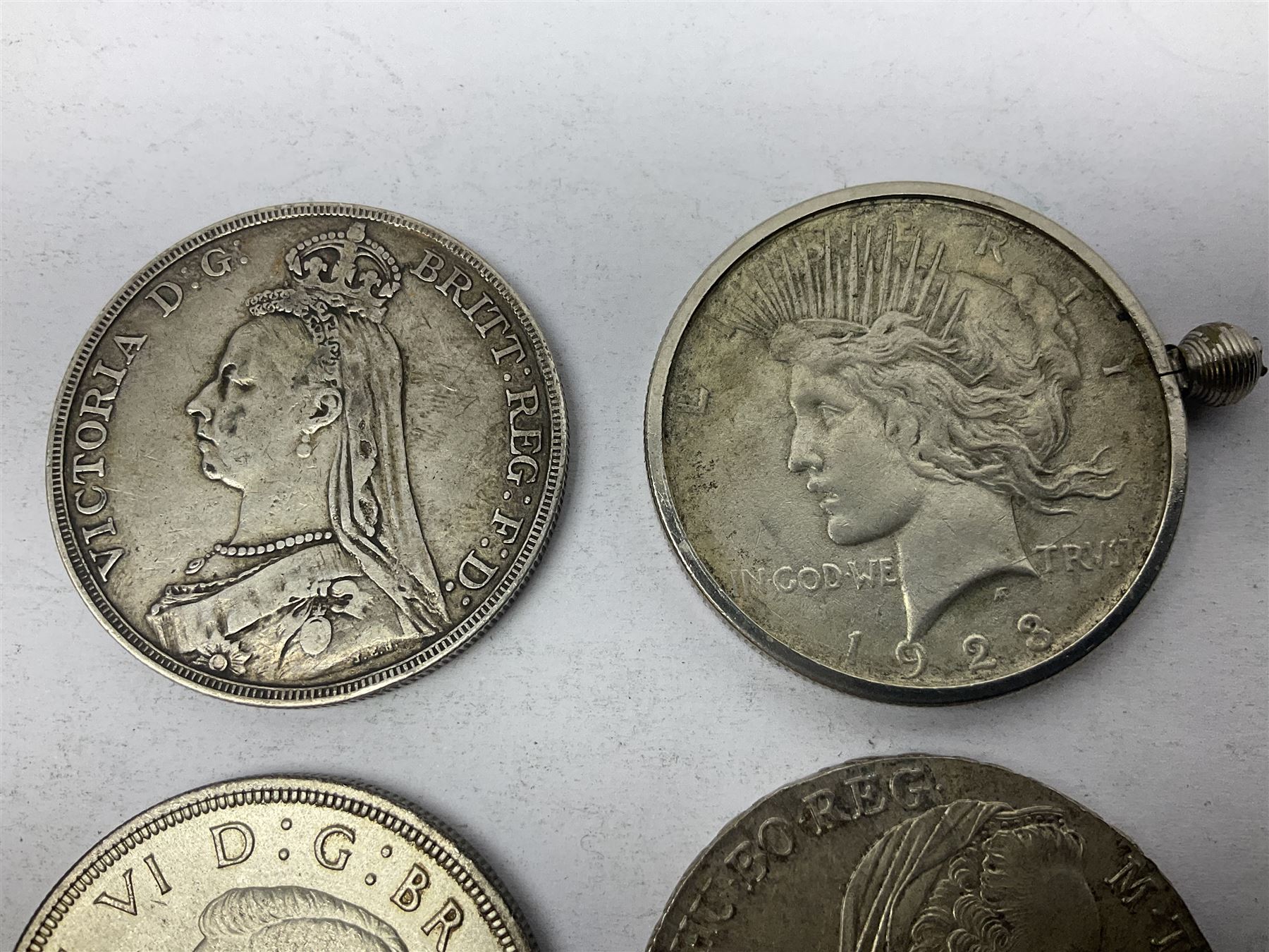 Four silver World coins comprising Queen Victoria 1889 crown, King George VI 1937 crown, Marie Thaler 1780 restrike, and mounted United States of America 1928 peace dollar 