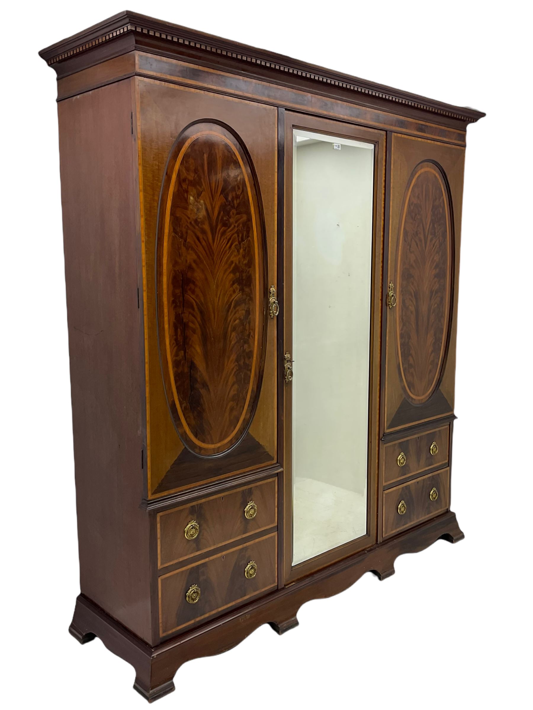 James Shoolbred & Co. London - Edwardian inlaid mahogany triple combination wardrobe, projecting dentil cornice over bevel glazed door, two figured oval panelled doors and four drawers, the central compartment fitted with linen slides and drawers, satinwood banding, on base with shaped apron and bracket feet, with enamel plaque 