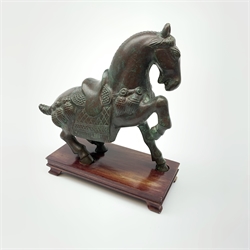 A bronze Tang style horse, modelled seated with one front leg raised, upon rectangular wooden base, bronze H20.5cm. 